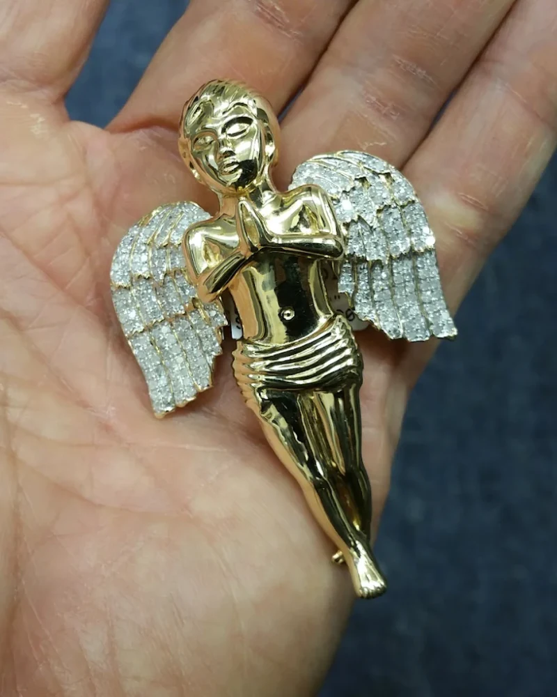 Solid gold praying angel pendant with diamond-set wings held in a palm