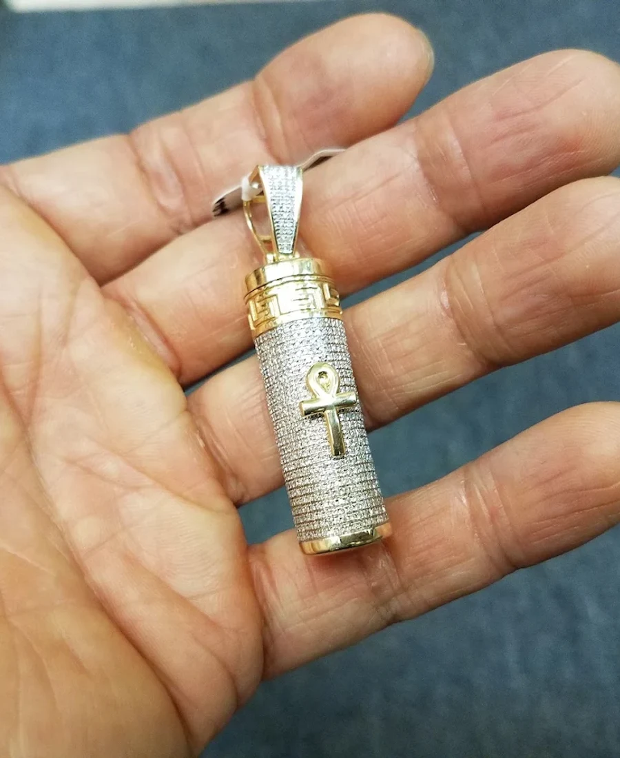 Iced-out ankh cylinder pendant with a gold bail held in a palm