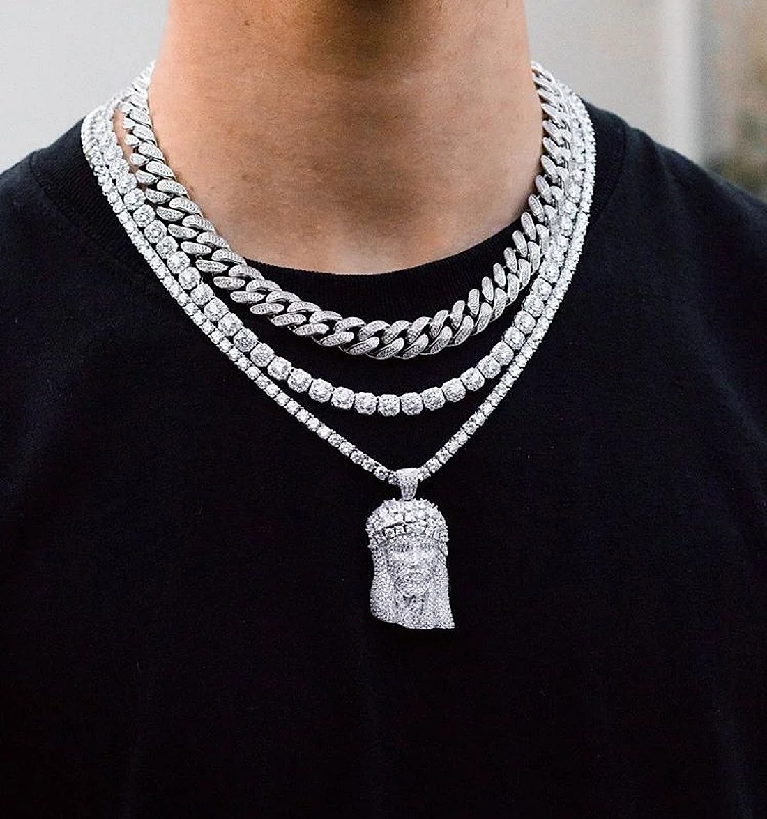 Man in a black tee wearing an iced Cuban link chain, a tennis chain and an iced pendant