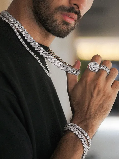 Man in a black tee wearing an iced silver Cuban chain with matching rings and bracelets