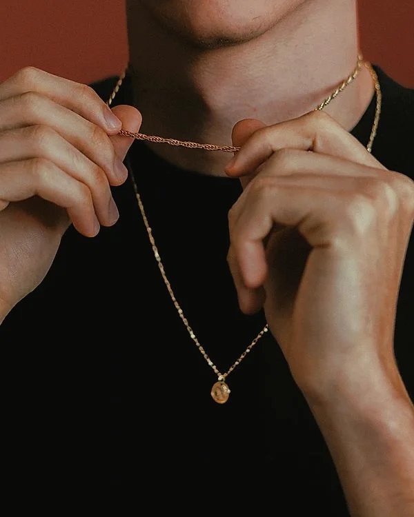 Man fastening a fine gold chain over a black tee