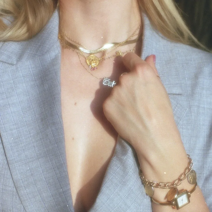 Gold watch and chain bracelet on a wrist in a gray blazer