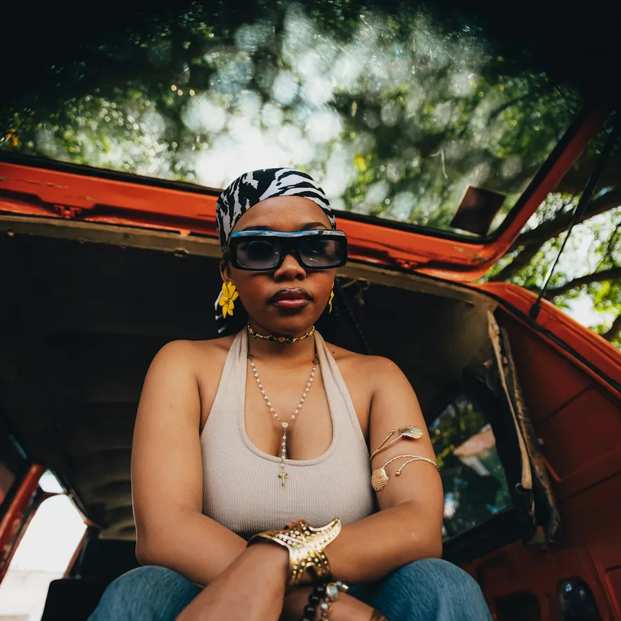Woman in sunglasses sitting in a vintage car wearing gold jewelry