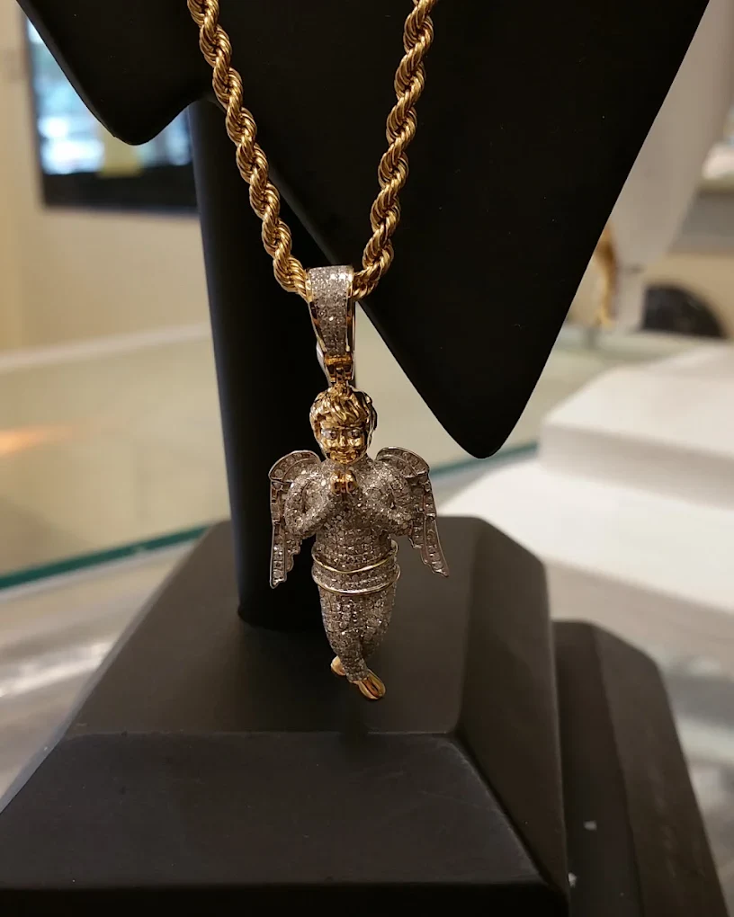 Iced-out angel pendant on a gold rope chain on a display stand at the counter
